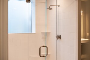 A glass-enclosed shower with a handheld showerhead, a glass door handle, and a window above the shower.