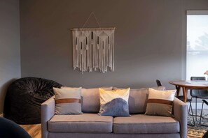 Ein modernes Wohnzimmer mit grauem Sofa, Wandbehang aus Makramee und einem Sitzsack.