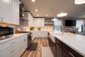A modern kitchen with white cabinets, stainless steel appliances, and pendant lighting. - Obsidian Shores Waterfront House on Crystal Lake with Private Beach Access (Beulah)