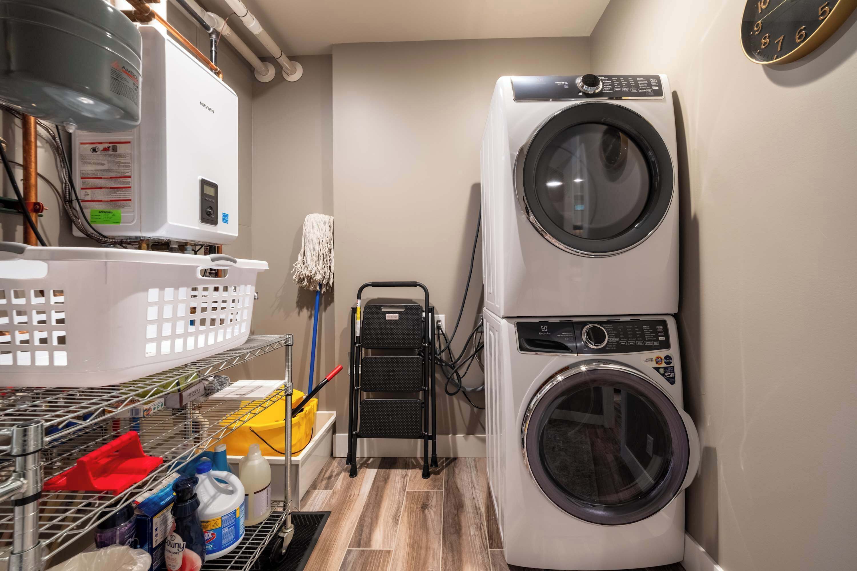 Une buanderie équipée d’un lave-linge et d’un sèche-linge superposés, d’un chauffe-eau et d’étagères contenant des produits de nettoyage.
