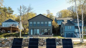 Ein modernes Haus mit Balkon, Steinmauer und drei Liegestühlen.