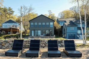 A modern house with a balcony, a stone wall, and three lounge chairs.