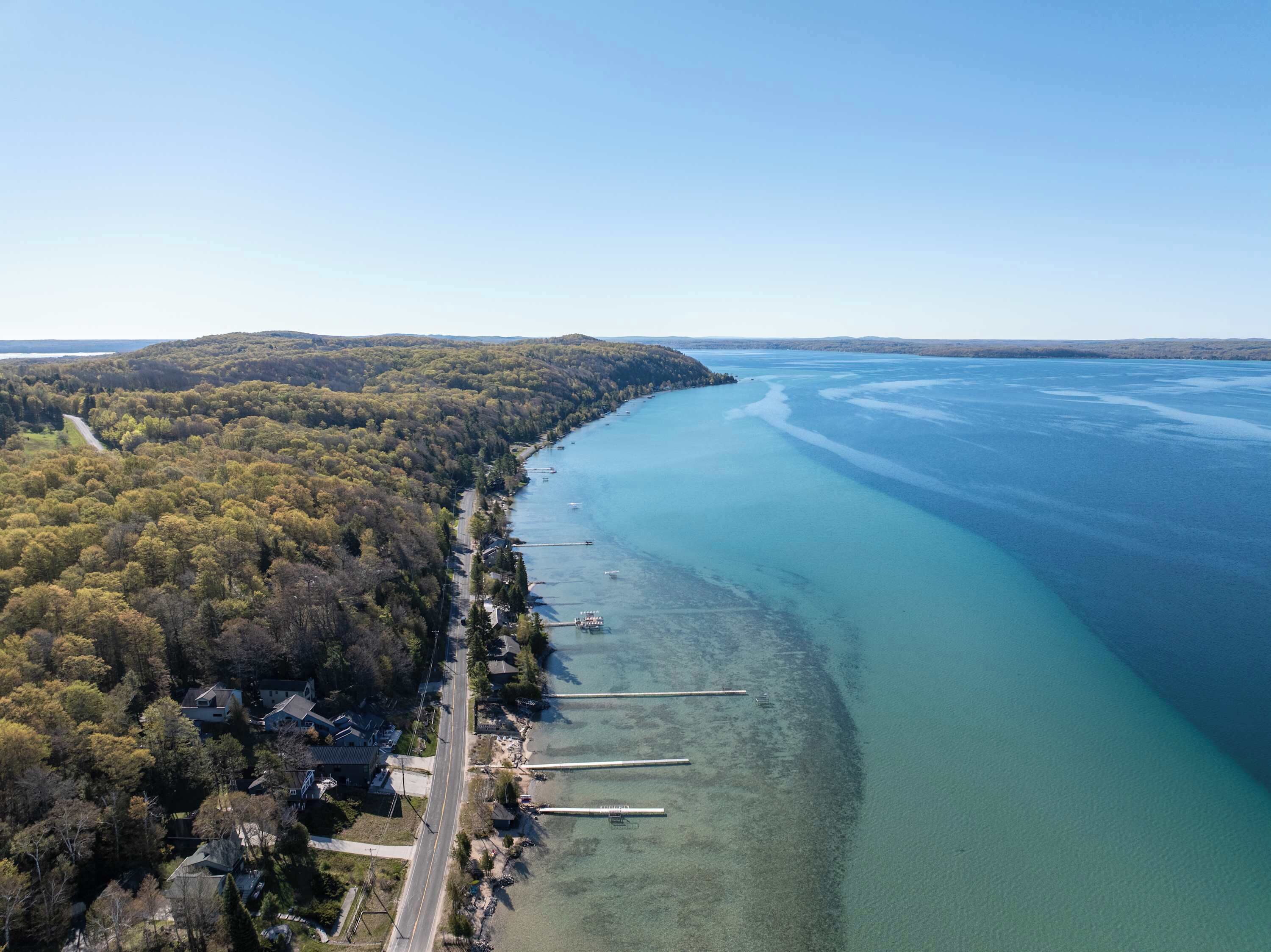 An aerial view of a coastal area with a road, houses, and docks along the shoreline.