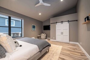 Ein Schlafzimmer mit Bett, Deckenventilator, Kleiderschrank, Sessel und Fenster.