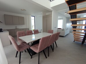 Una cocina moderna con armarios blancos, un comedor con mesa blanca y sillas estampadas, y una escalera con escalones de madera.