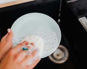 A hand holding a bowl with a sponge, washing dishes in a kitchen.
