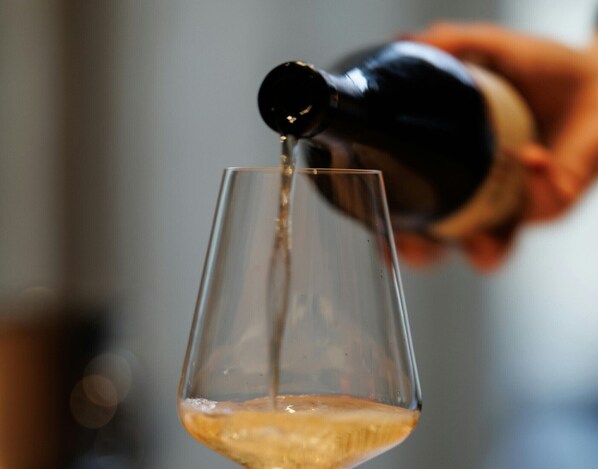 A hand pouring a liquid into a clear glass.