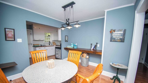 A dining area with a round table, wooden chairs, a kitchen in the background, and a small side table with a lamp. - Welcome to the Honey House in beautiful Hampton South Carolina (Hampton)