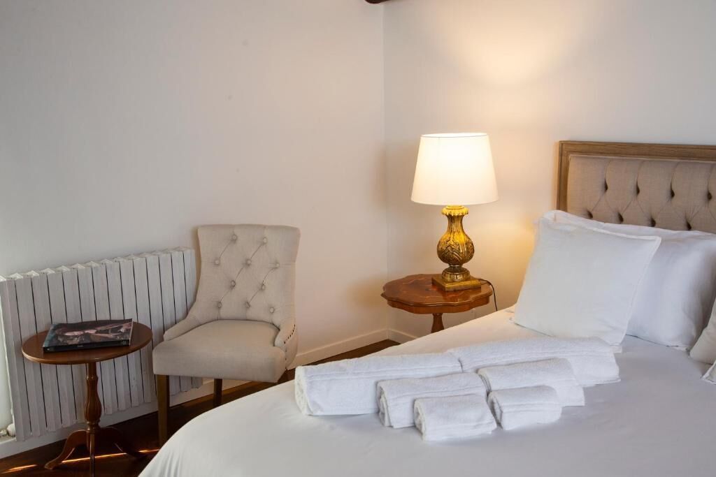 A hotel room with a bed, a chair, a table, a lamp, and a radiator.