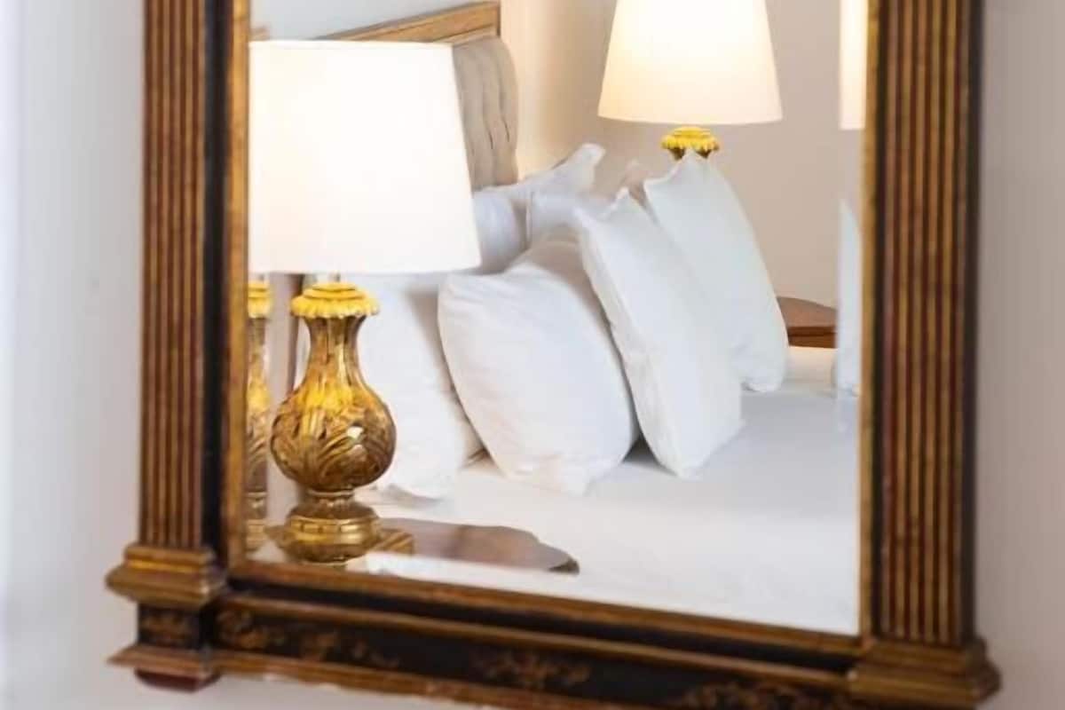 A mirror with a wooden frame, reflecting a bed with white bedding and two lamps.