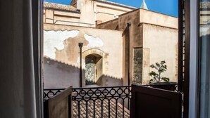 A balcony with a wrought iron gate, a view of a building with a tiled roof, and a clear blue sky. - Dimora Sinibaldi (Palermo)