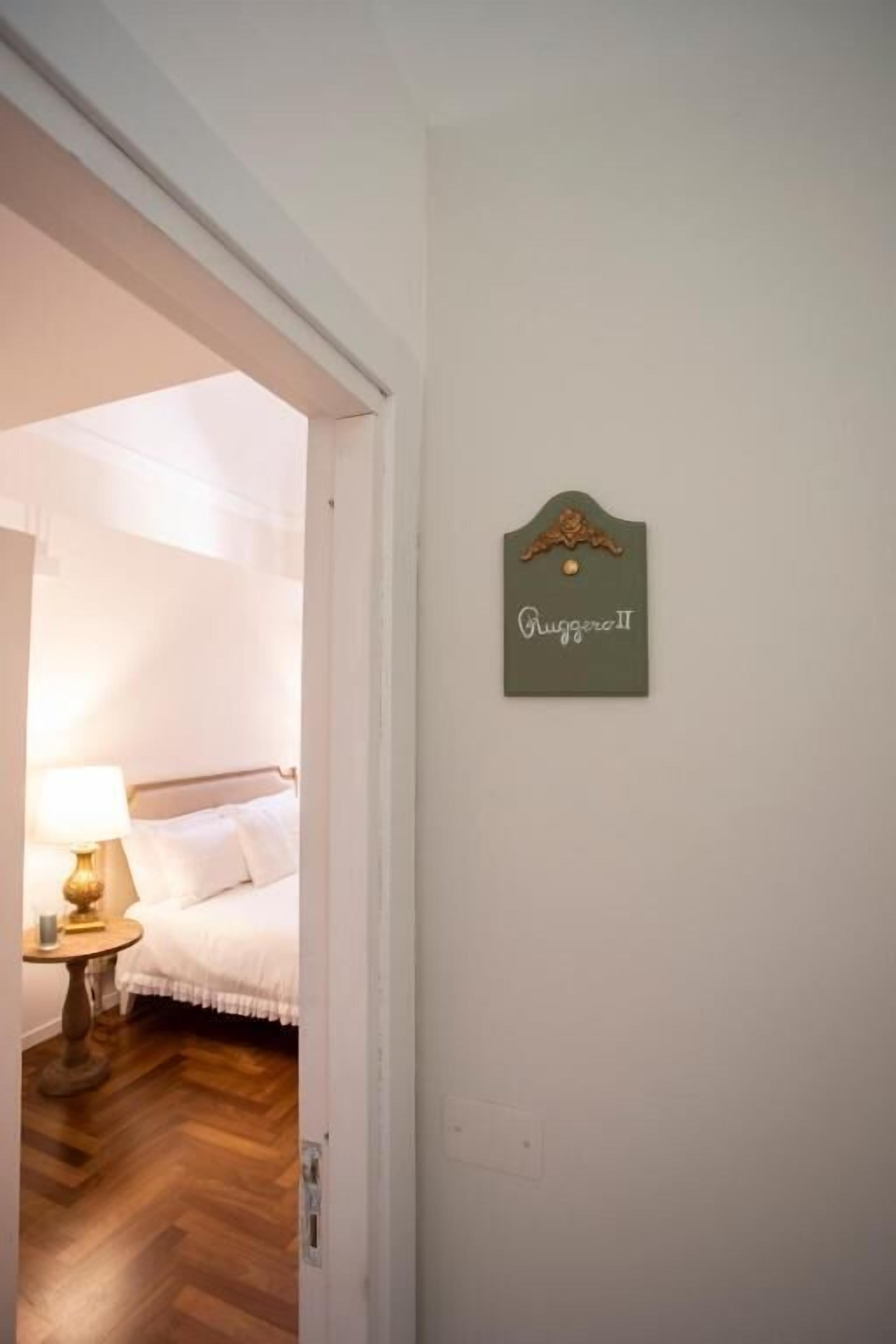 A hotel room with a bed, a bedside table with a lamp, and a sign on the wall.