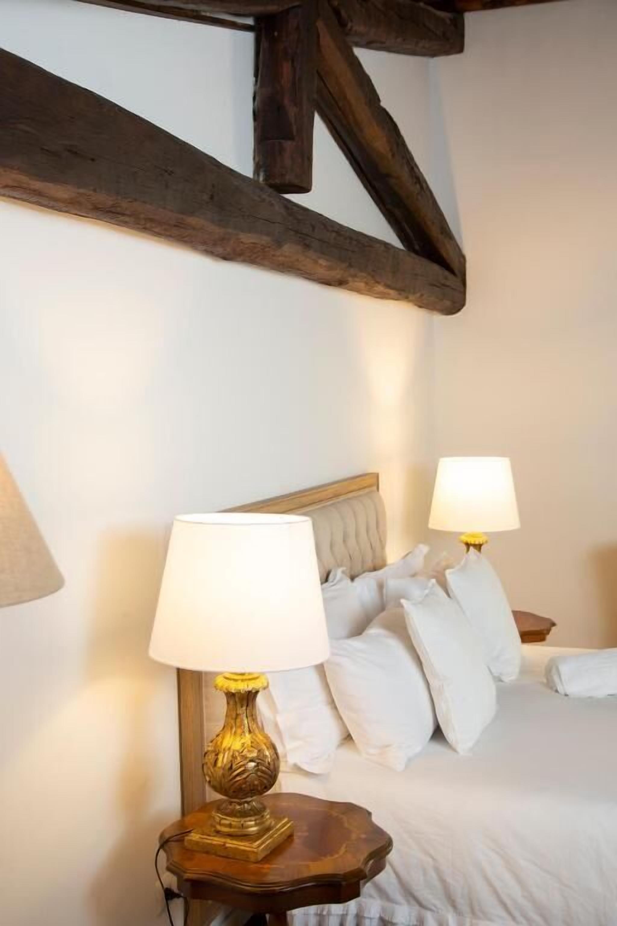 Un dormitorio con cama, dos lámparas de noche y vigas de madera a la vista.