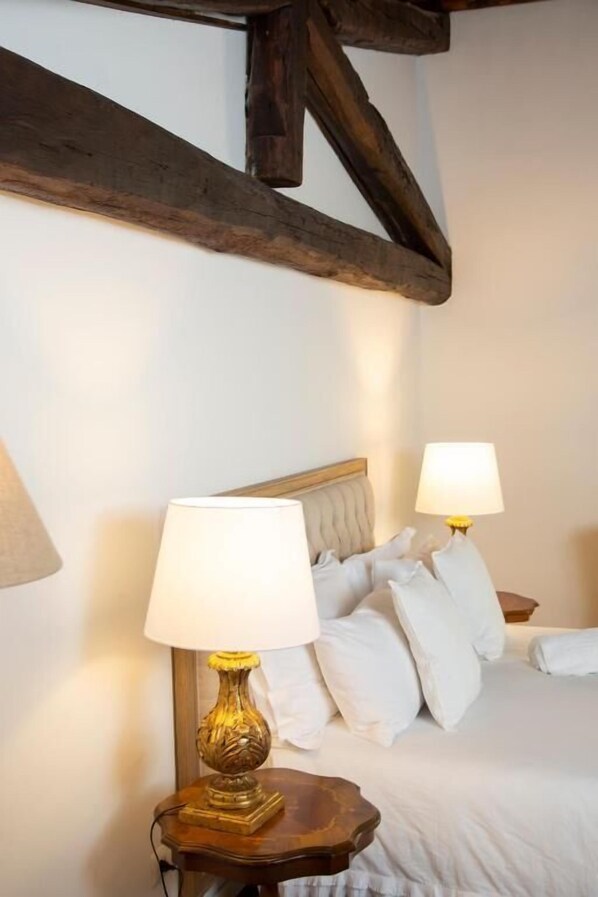 A bedroom with a bed, two bedside lamps, and exposed wooden beams. - Dimora Sinibaldi (Palermo)