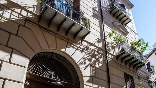 A building with a large arched entrance, multiple balconies with plants, and a sign above the door. - Dimora Sinibaldi (Palermo)