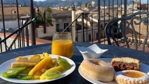 A table with a plate of fruit, a glass of orange juice, and pastries, overlooking a mountainous landscape. - Dimora Sinibaldi (Palermo)