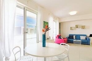 Un salón luminoso con una mesa redonda, sillas blancas, un sofá azul y una silla rosa.