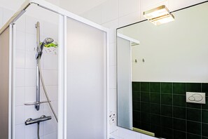 Un bany amb dutxa, mirall i un llum penjada a la paret.