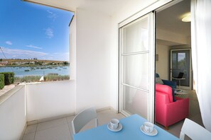 Un balcón con vista a un lago, una mesa con dos tazas y una silla roja.