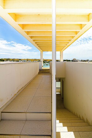 Un corredor exterior cubierto con vistas al mar y edificios lejanos.