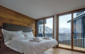 Un dormitorio con cabecera de madera, una cama grande y un balcón con vista a árboles nevados.