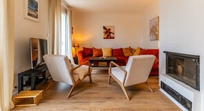 A living room with a sofa, two armchairs, a TV, a fireplace, and artwork on the walls. - Large house with garage, little corner of greenery, close to the center of Dijon (Talant)