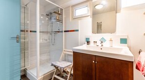 Een badkamer met een douche, een wastafel met toiletartikelen en een spiegel.