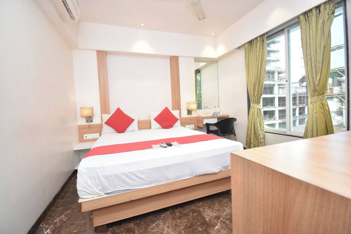 A hotel room with a bed, bedside tables, a desk, a chair, and a large window with curtains.