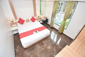 A hotel room with a bed, a desk, a chair, a lamp, and a window with curtains. - Hotel Royal Oak (Navi Mumbai)