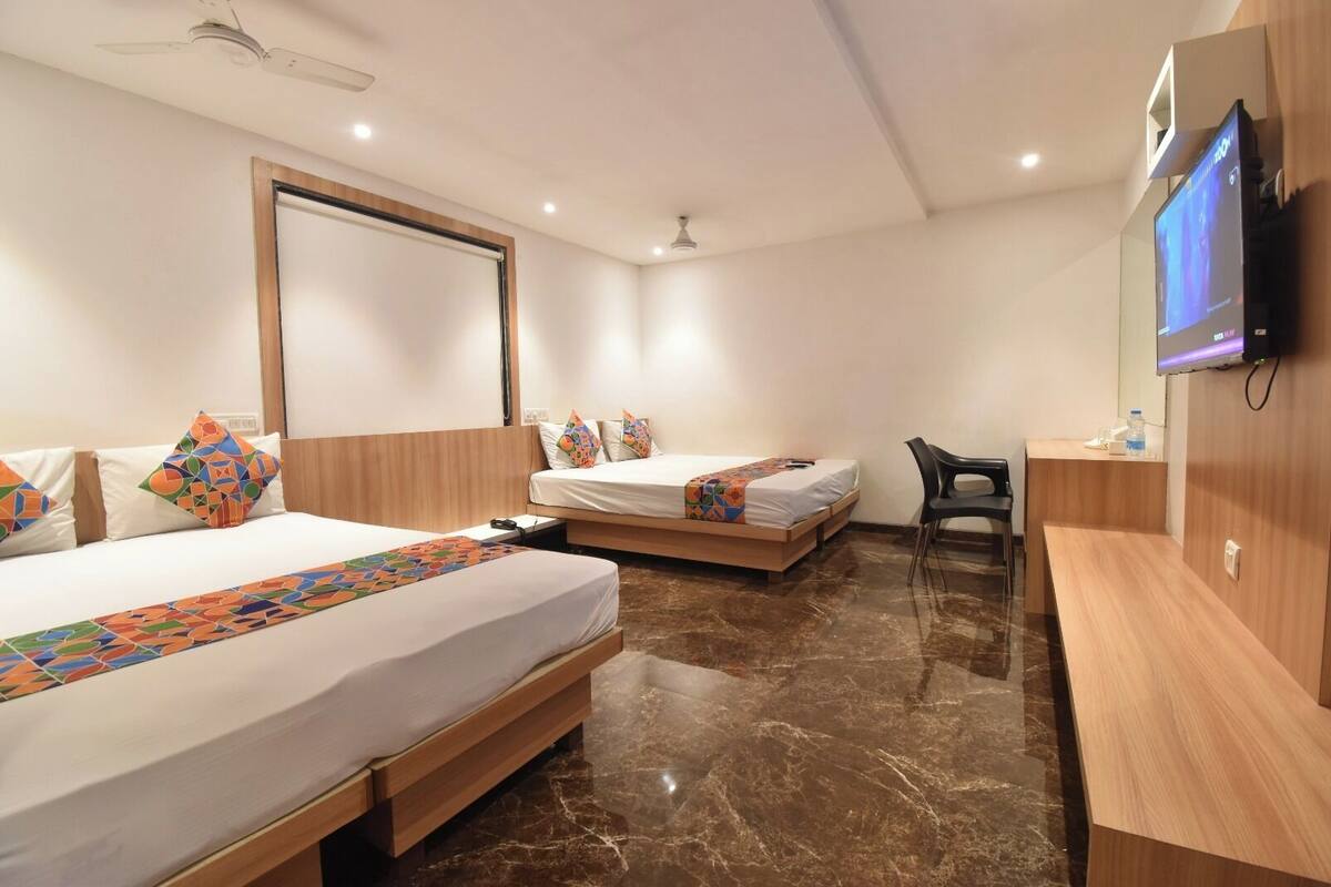 A hotel room with two beds, a desk, a chair, a television, and a ceiling fan.