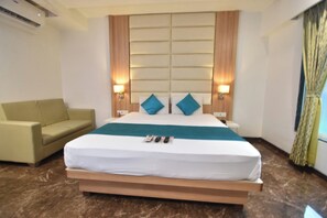 A hotel room with a large bed, a sofa, and two bedside lamps. - Hotel Royal Oak (Navi Mumbai)