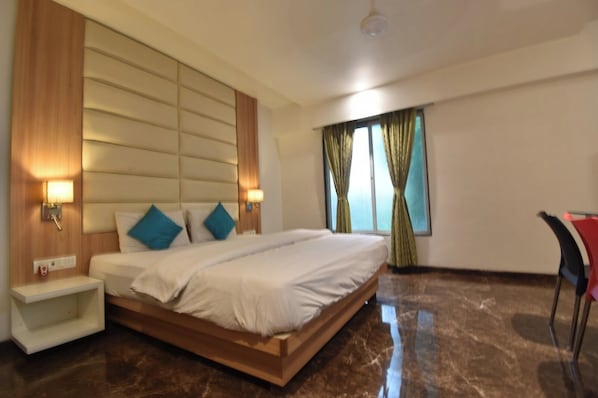 A modern hotel room with a large bed, bedside lamps, a nightstand, a chair, and a window with curtains. - Hotel Royal Oak (Navi Mumbai)
