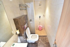 A bathroom with a toilet, a sink, a mirror, and a shower area. - Hotel Royal Oak (Navi Mumbai)