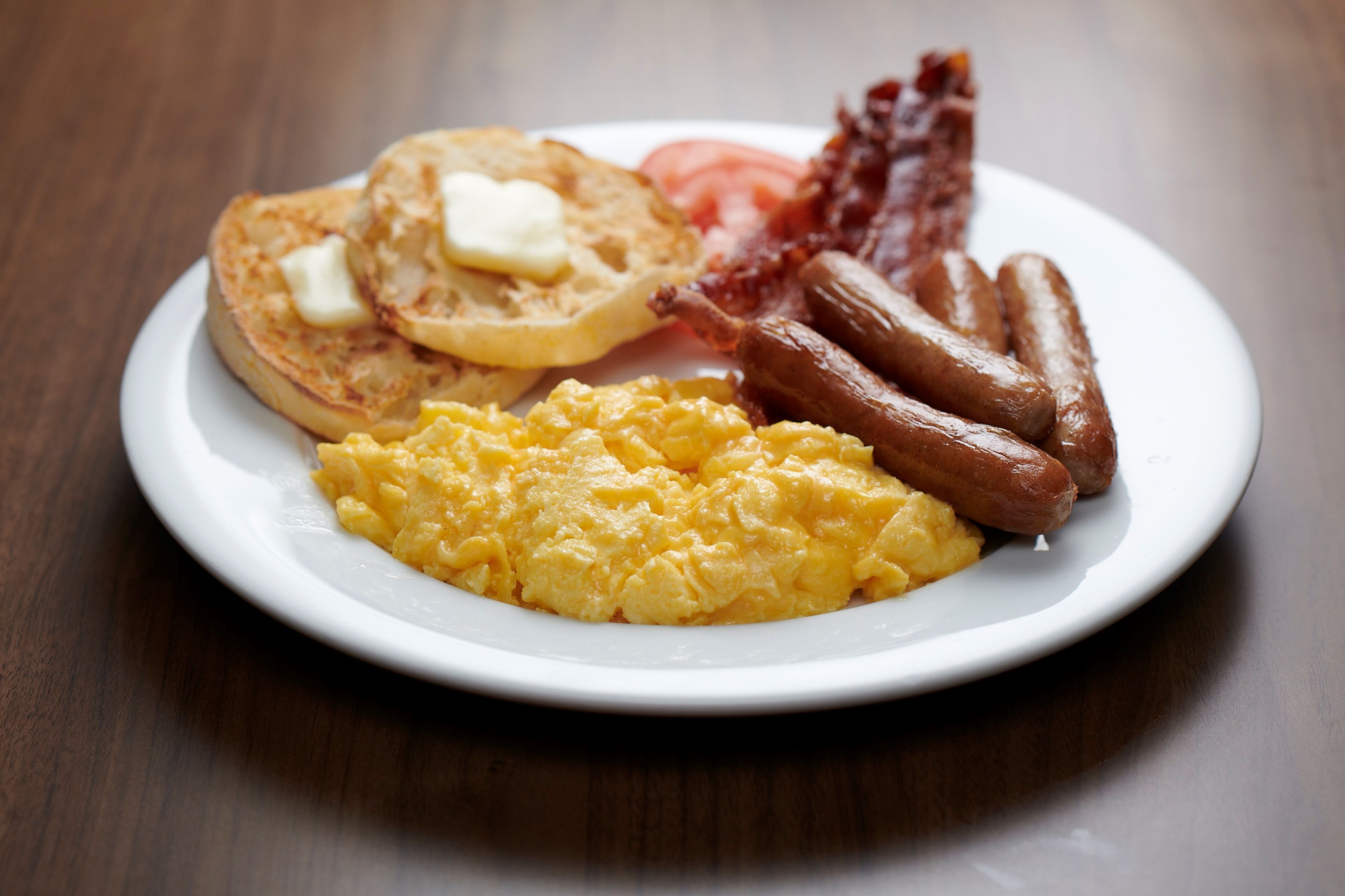 Une assiette avec des œufs brouillés, des saucisses, du bacon et des toasts beurrés.
