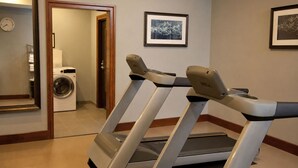 Un gimnasio en casa con cintas de correr, una lavadora y un espejo que refleja la habitación.