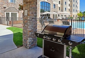 A stone pillar, a barbecue grill, a pool, and a building with multiple windows.