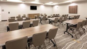 Une salle de conférence équipée de plusieurs tables et chaises, d’un téléviseur à écran plat fixé au mur et d’un panneau en bois sur le mur du fond.