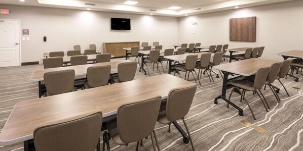 A conference room with multiple tables and chairs, a flat-screen TV mounted on the wall, and a wooden panel on the back wall.