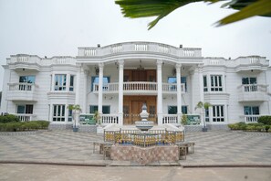 Un grand bâtiment blanc, doté d’une entrée centrale, de nombreux balcons et d’une fontaine dans la cour.