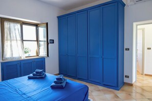 Une chambre avec une grande armoire bleue, un lit avec une literie bleue et une fenêtre ornée de rideaux légers.