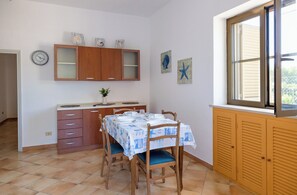 Une cuisine avec une table à manger, des chaises, des meubles de rangement en bois, une horloge et des œuvres d’art accrochées aux murs.