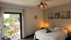 Un dormitorio con cama, lámparas de noche, un reloj de pared, un cuadro de Buda y vistas del patio exterior.