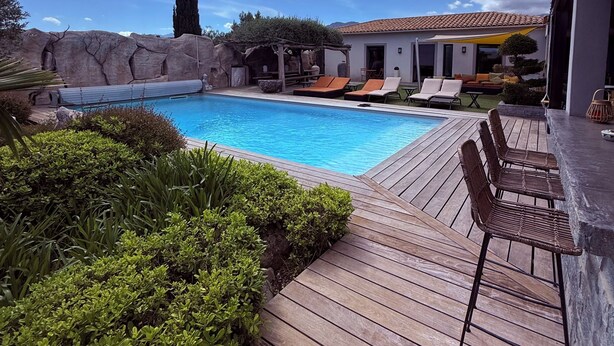 Una piscina con terraza de madera, sillas de descanso y una pérgola.