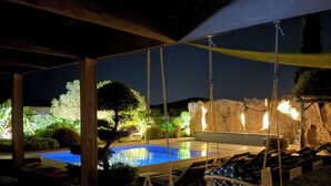 Un área de piscina al aire libre con una silla hamaca, un muro de piedra y una lámpara colgante.