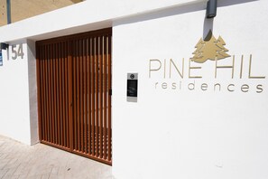 A building entrance with a wooden gate, the number 154, and the name 'Pine Hill Residences' with a pine tree logo. - Pine Hills - New Apartment Fuengirola (Fuengirola)