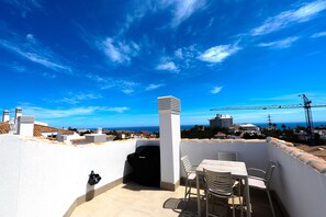 A rooftop terrace with a table and chairs, a grill, and a view of the city and sea. - Pine Hills - New Apartment Fuengirola (Fuengirola)