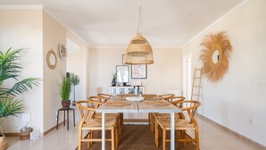 A dining area with a wooden table, wicker chairs, and a hanging light fixture. - Villa Sabine - Spectacular Sea View Villa in Capel (Benalmádena)
