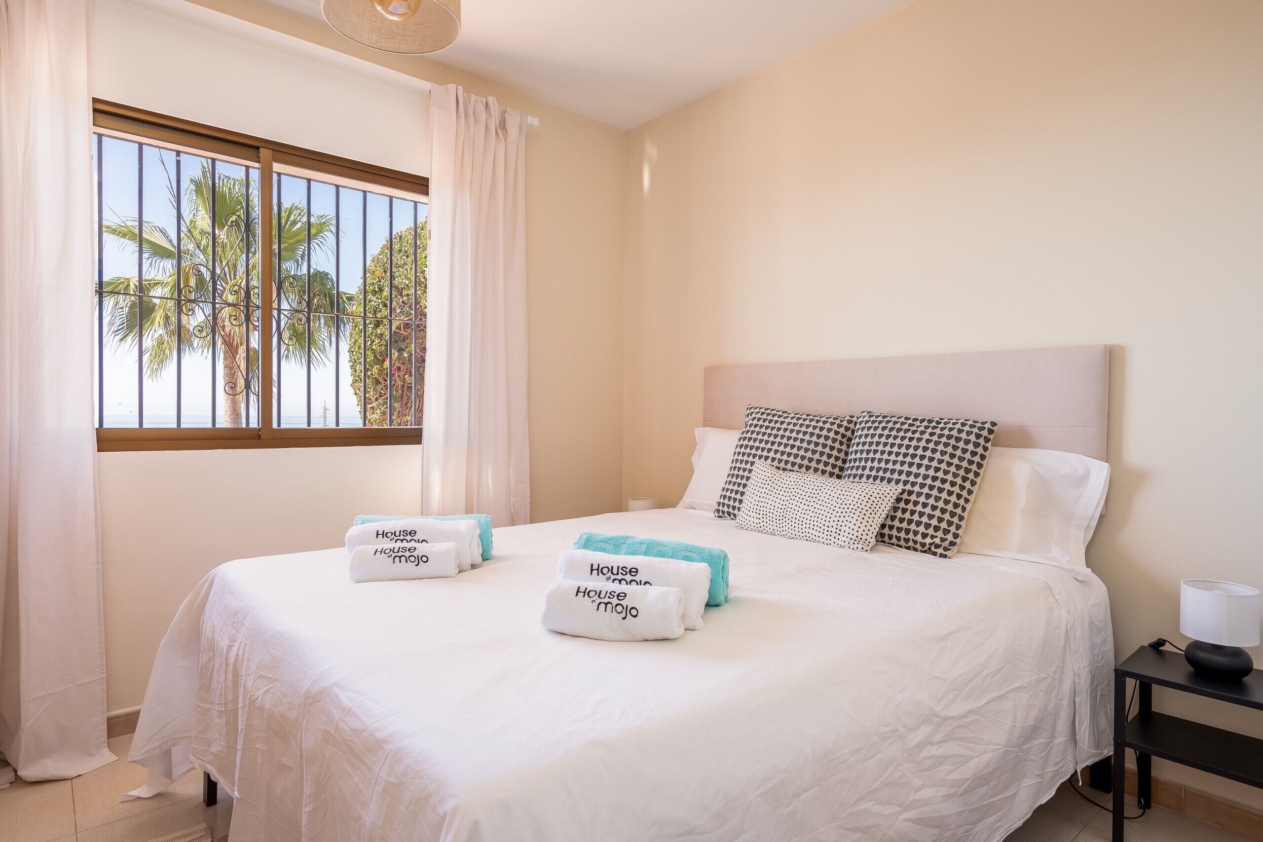 A hotel room with a bed, pillows, a nightstand, and a window with curtains.
