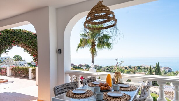 A dining table with plates, cups, and a bottle, set against a scenic view of the sea and hills. - Villa Sabine - Spectacular Sea View Villa in Capel (Benalmádena)