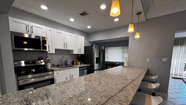 A modern kitchen with granite countertops, stainless steel appliances, and pendant lighting. - Charming 3-bedroom house in Tamarac. Minutes from Hardrock, Beaches, & Shopping (Tamarac)
